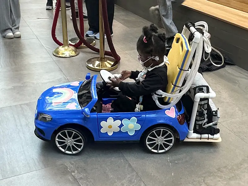 A young child using her GoBabyGo car with her portable oxygen supply onboard.