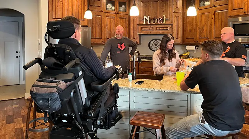 Lonnie spending time with friends at a kitchen island with his seat elevated