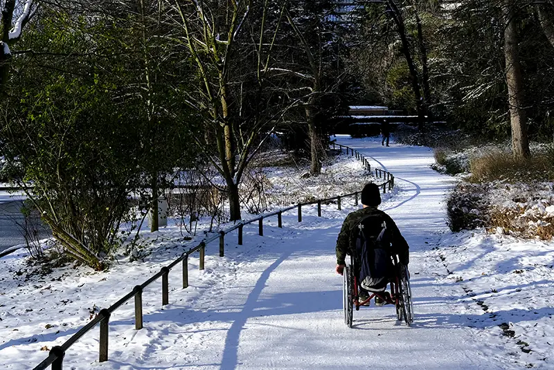 A man pushes his wheelchair through a snow-covered trail in a park