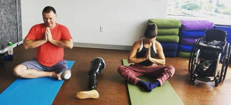 A man with an amputation and a woman who uses a wheelchair practicing yoga